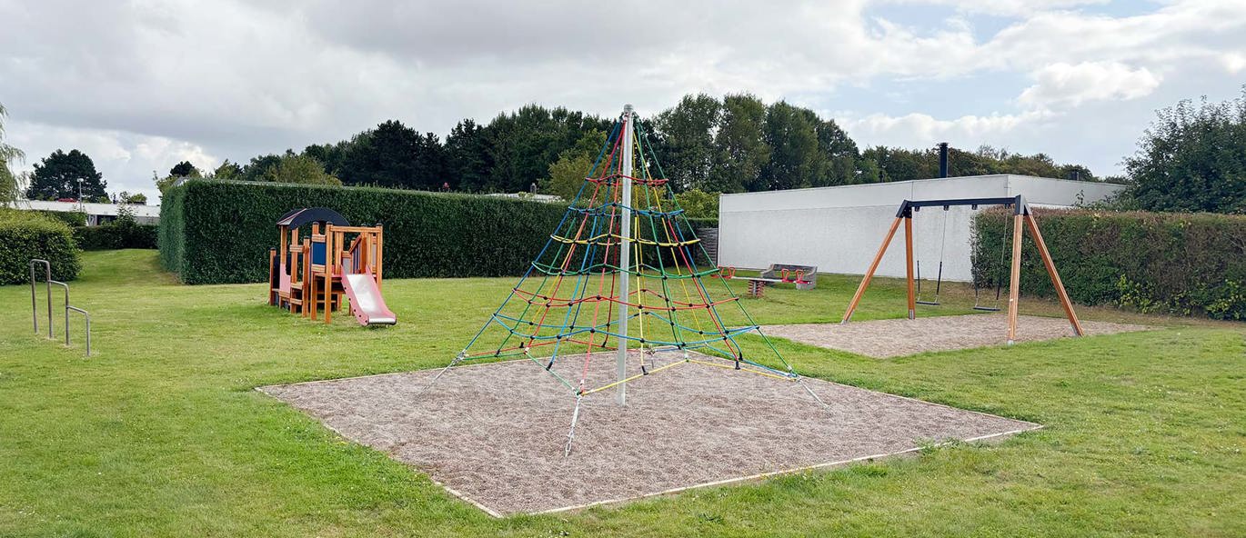 Legeplads i grønt område med klatrestativ, fugleredegynge og legestativ som lokomotiv