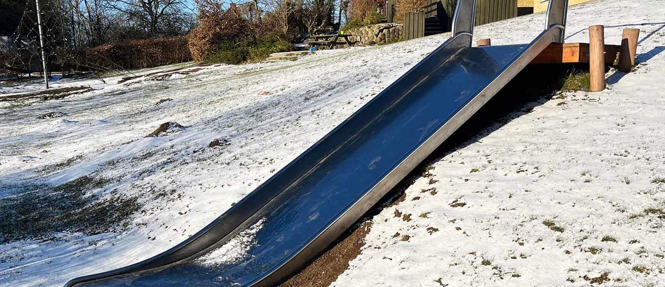 rutsjebane i stål på bakke dækket af sne med gul skole i baggrunden